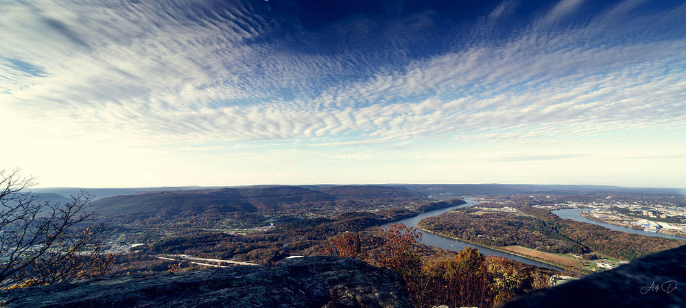 Overlook above a winding river valley and town under streaked clouds