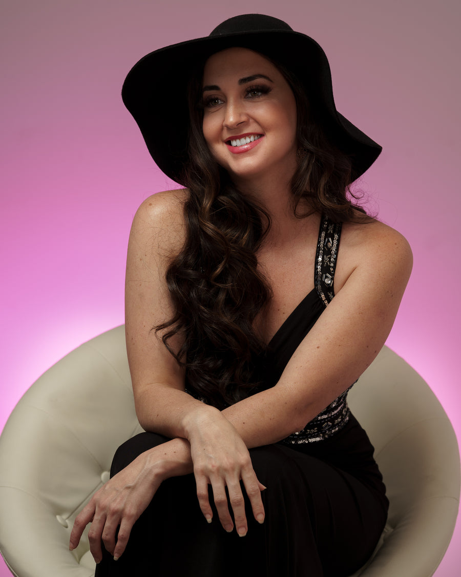 Studio portrait of a woman in a wide-brimmed black hat against a magenta backdrop