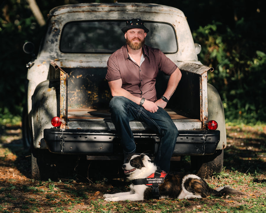 Outdoor portrait of a man seated on the tailgate of a weathered pickup with his dog