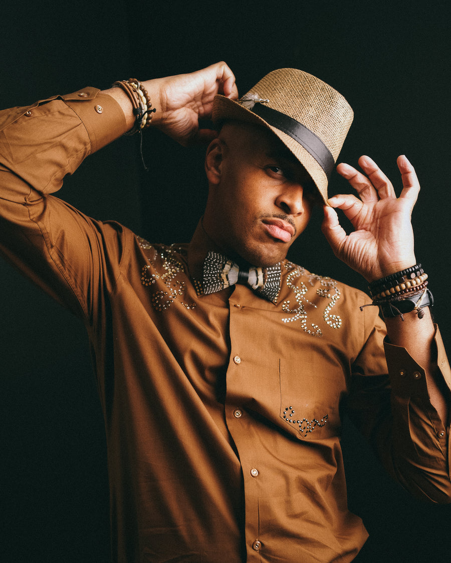 Western-styled portrait of a man in a camel shirt and bolo tie tipping his hat