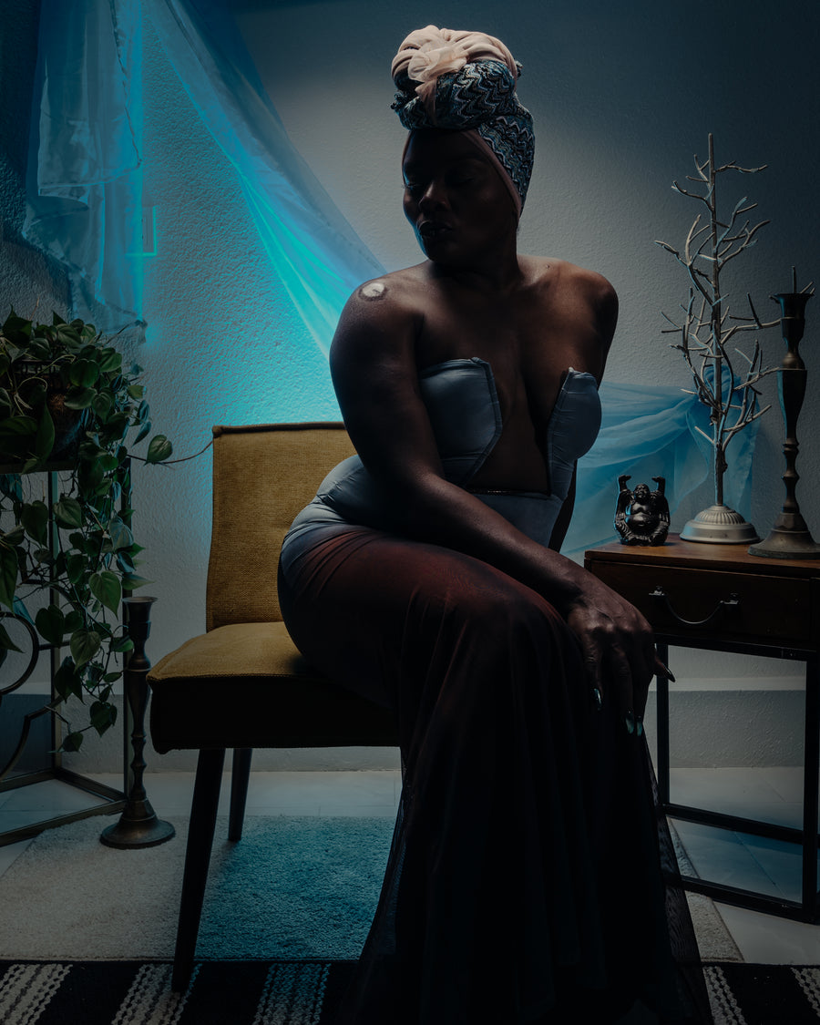 Environmental portrait of a seated figure in a room lit teal and gold