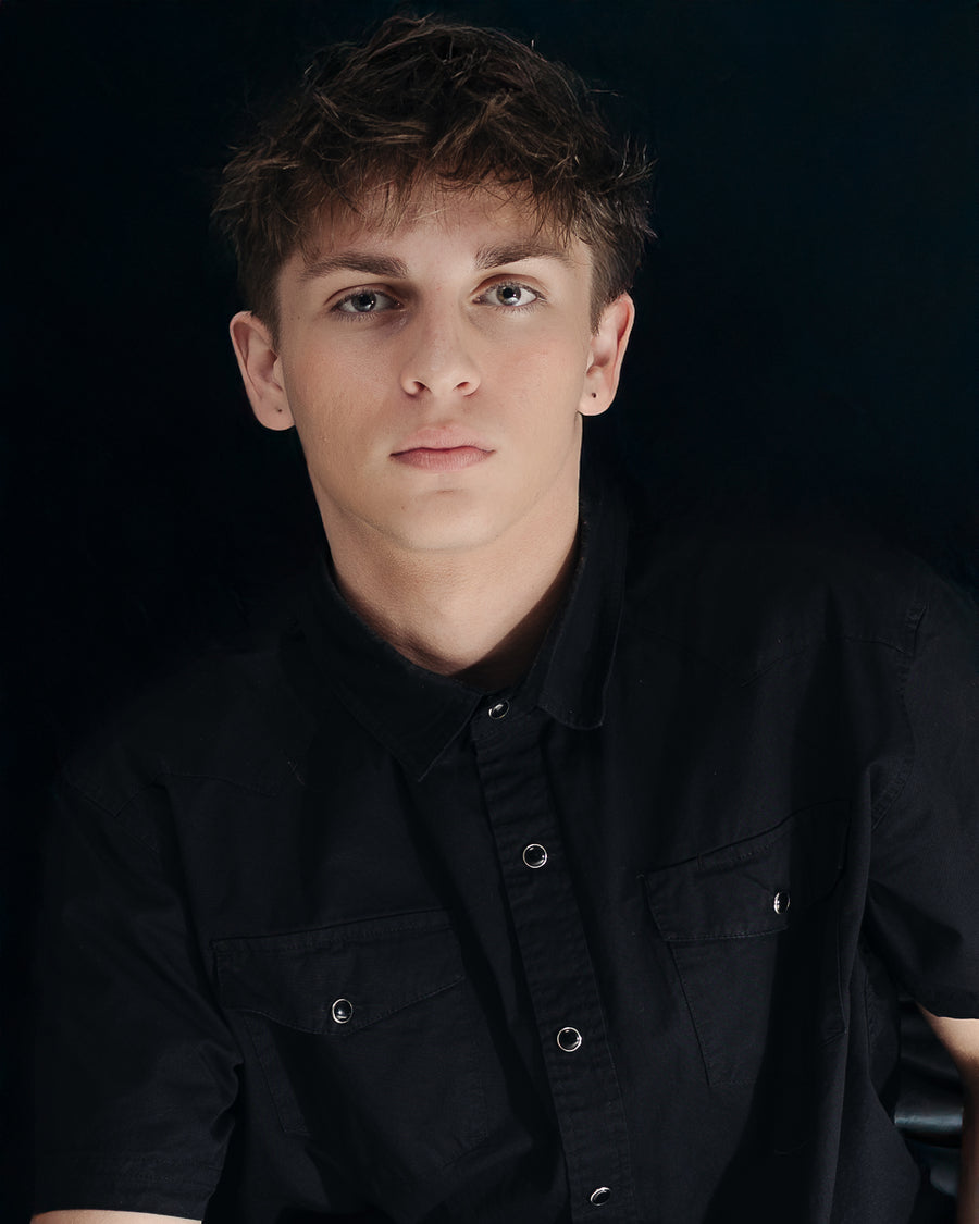 Dark studio headshot of a young man in a black shirt