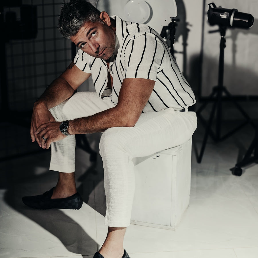Editorial portrait of a man in a striped shirt seated on a white block