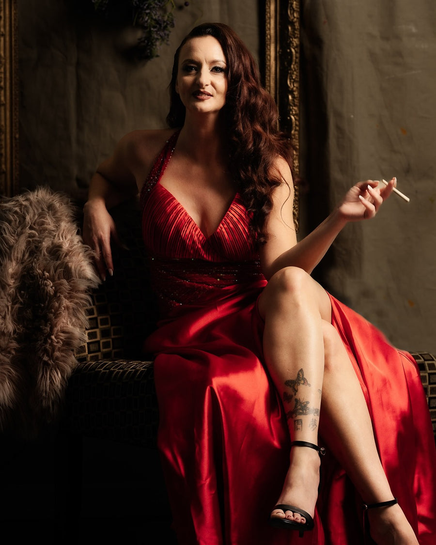 Portrait of a woman in a red gown seated in an ornate, dimly lit room